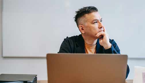 A man sitting in front of a laptop and thinking.