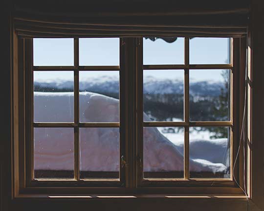 A window looking out on snowy mountains with a large pile of snow in front of it