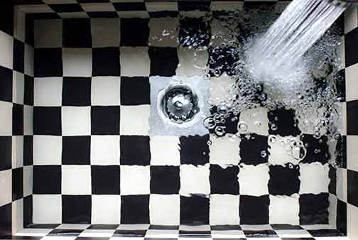 A clean black and white kitchen sink being cleaned to avoid drain clogs.