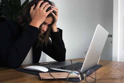 A person looking stressed while looking for an emergency plumber on her laptop.