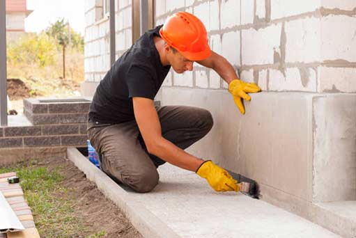 a worker performing exterior waterproofing on a home.